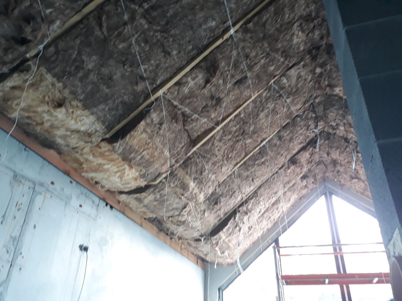 Montaż izolacji z wełny mineralnej na poddaszu, widoczne drewniane belki stropowe i luźno wiszące przewody.