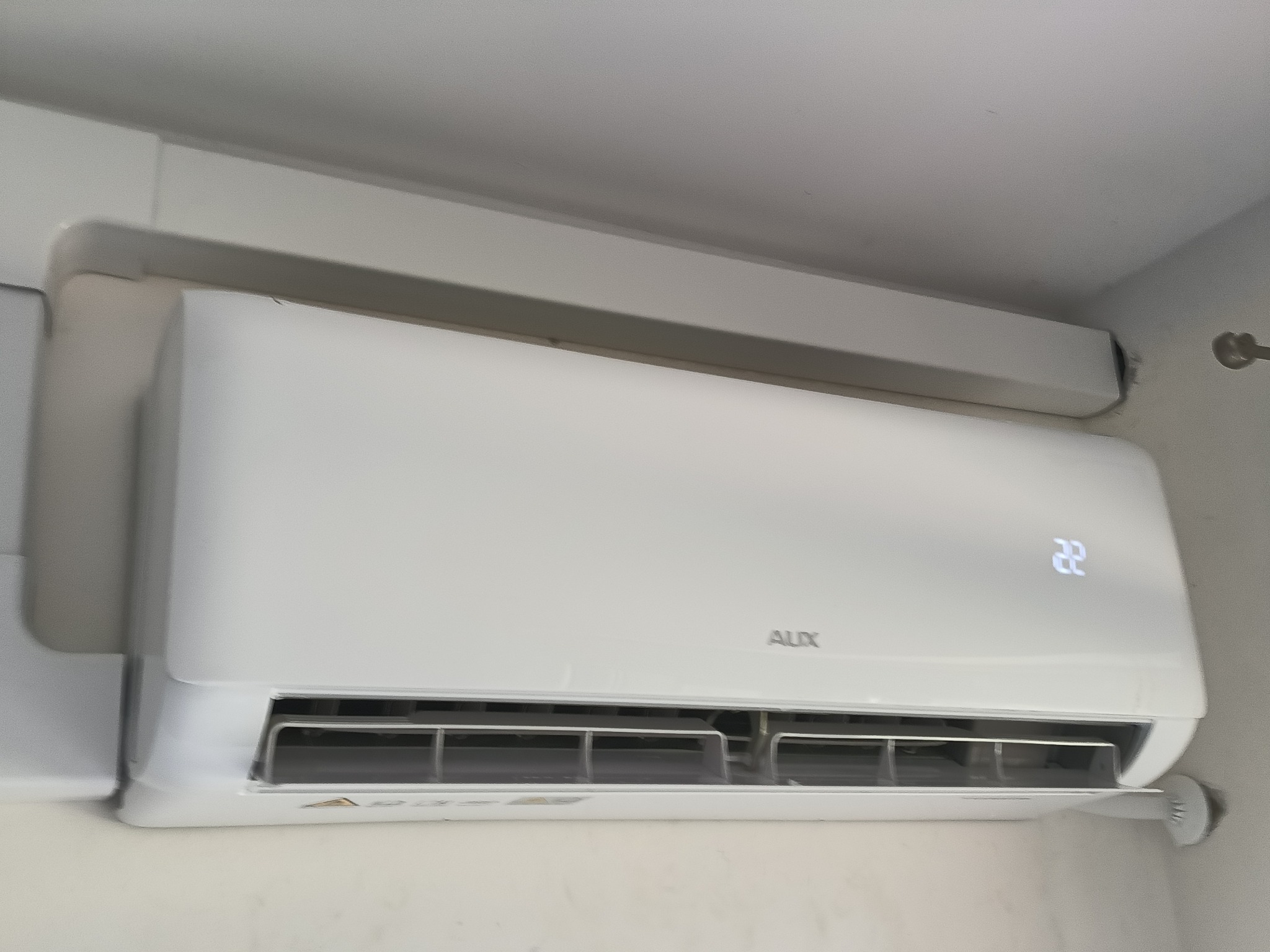 Biała klimatyzacja AUX zamontowana pod sufitem, wyświetlająca temperaturę 22 stopnie Celsjusza.