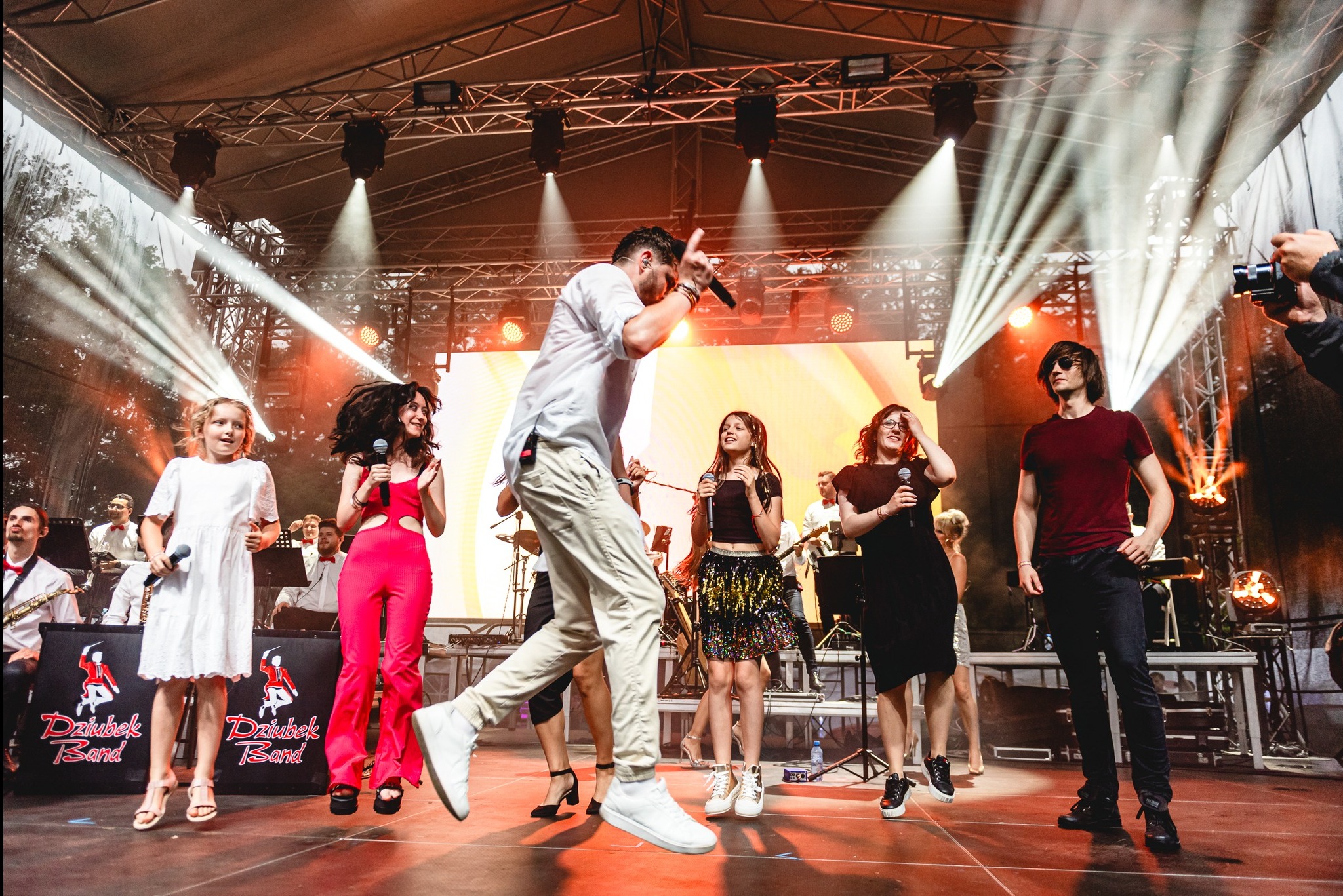 Zespół muzyczny Dziubek Band na scenie podczas występu, wokalista w ruchu, oświetlenie sceniczne, publiczność w tle.