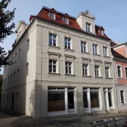 Odnowiona kamienica w Szczytnie, z jasną elewacją, czerwonym dachem i białymi oknami, widziana z perspektywy ulicy.