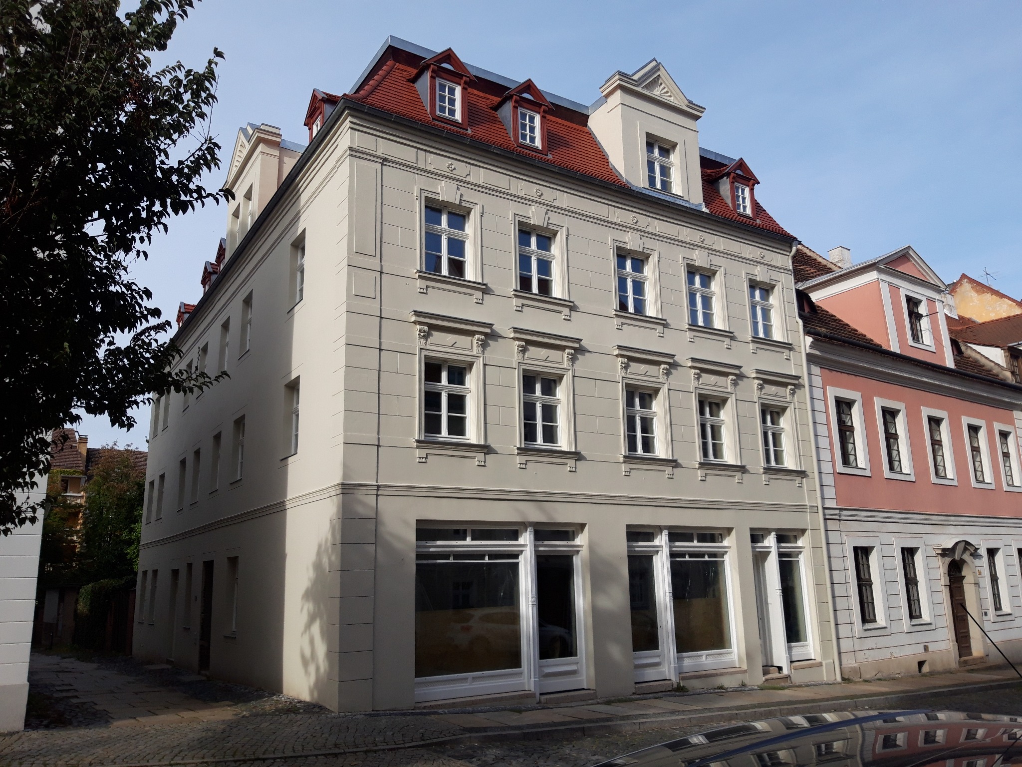 Odnowiona kamienica w Szczytnie, z jasną elewacją, czerwonym dachem i białymi oknami, widziana z perspektywy ulicy.