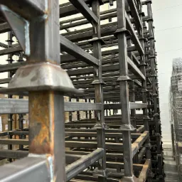 Metalowa konstrukcja regałowa z profili kwadratowych, spawana, z widocznymi śladami rdzy, ułożona w magazynie.