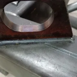 Szczegółowe ujęcie spoiny łączącej metalowy element z otworem, wykonanej na konstrukcji ze stali, widoczne ślady obróbki.