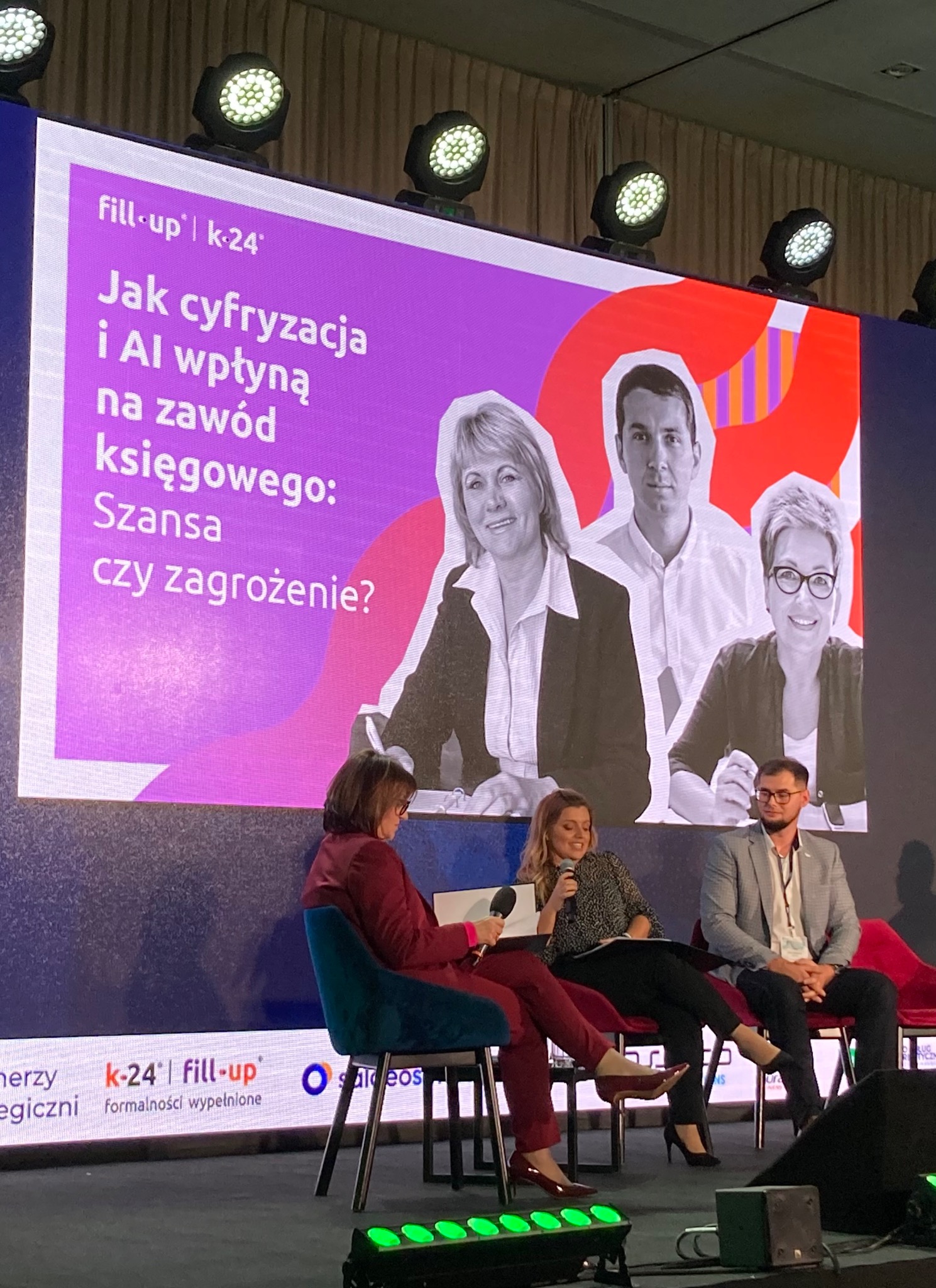 Konferencja o cyfryzacji w księgowości: panel dyskusyjny z prelegentami na scenie, w tle wyświetlany slajd z pytaniem o wpływ AI na zawód księgowego, oświetlenie sceniczne.