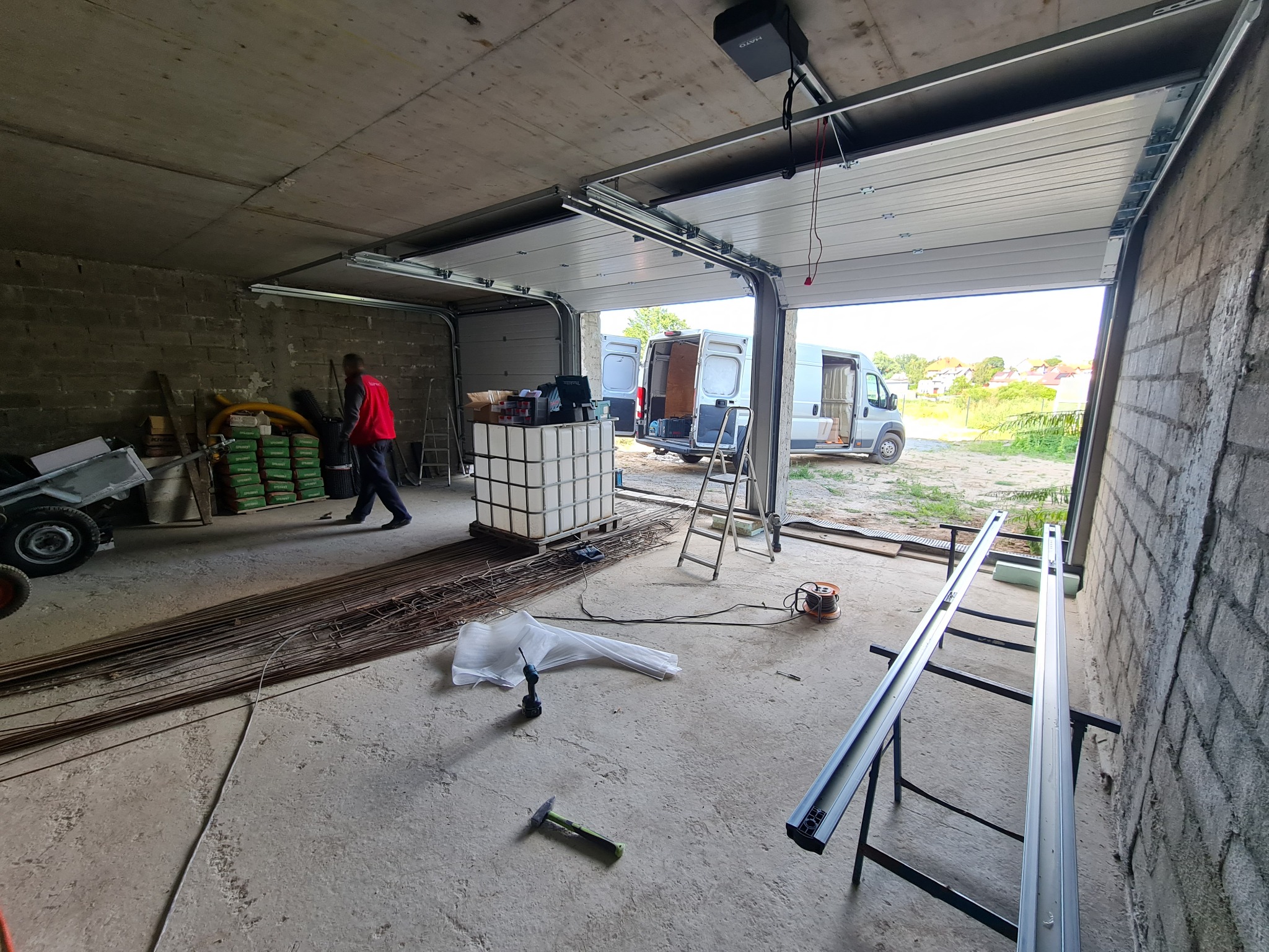 Montaż segmentowej bramy garażowej z napędem elektrycznym w surowym garażu, widoczna furgonetka na zewnątrz