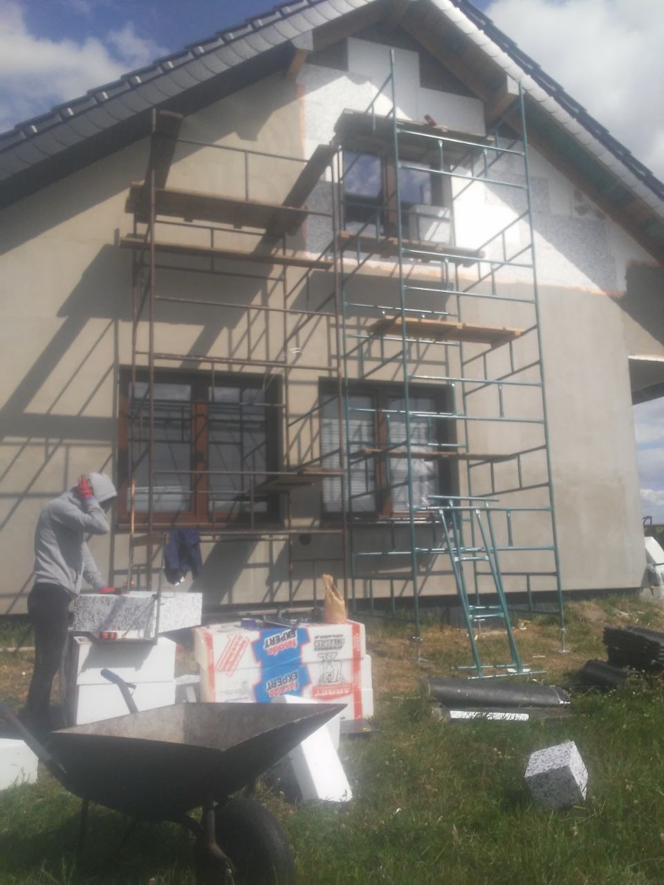 Prace przy ocieplaniu domu jednorodzinnego w Częstochowie, widoczne rusztowanie, styropian i pracownik przygotowujący materiał.