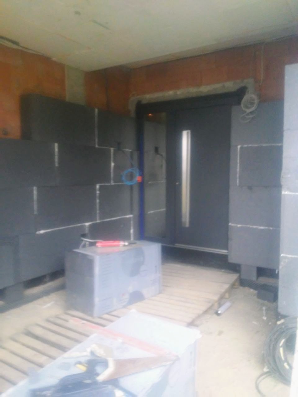 Ocieplanie elewacji styropianem grafitowym wokół drzwi wejściowych, widoczne narzędzia i materiały budowlane.