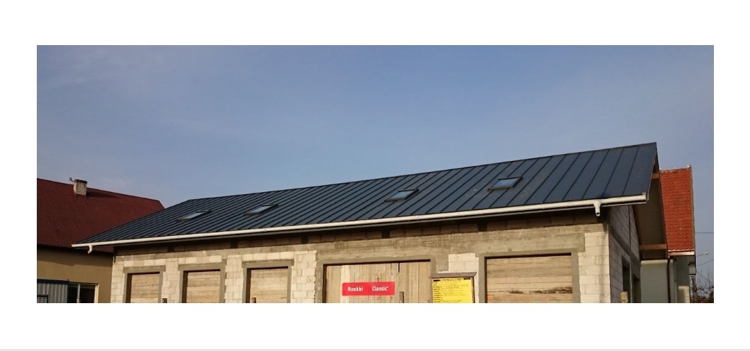 Nowoczesny dach z blachy na budynku w trakcie budowy, widoczne okna dachowe i orynnowanie, z tabliczką producenta Ruski Classic.