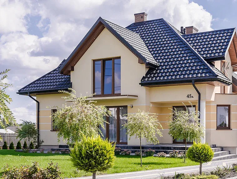Nowoczesny dom jednorodzinny z ciemnym dachem z metalowych paneli na tle błękitnego nieba z chmurami, widoczne rynny i numer domu 45A.