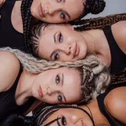 Portret czterech modelek z różnymi kolorami włosów i fryzurami w czarnych topach leżących blisko siebie na jasnym tle, z subtelnym makijażem i wyrazistymi oczami.