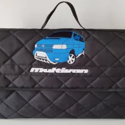 Czarna, pikowana torba z haftowanym niebieskim vanem i napisem 'Multivan'.