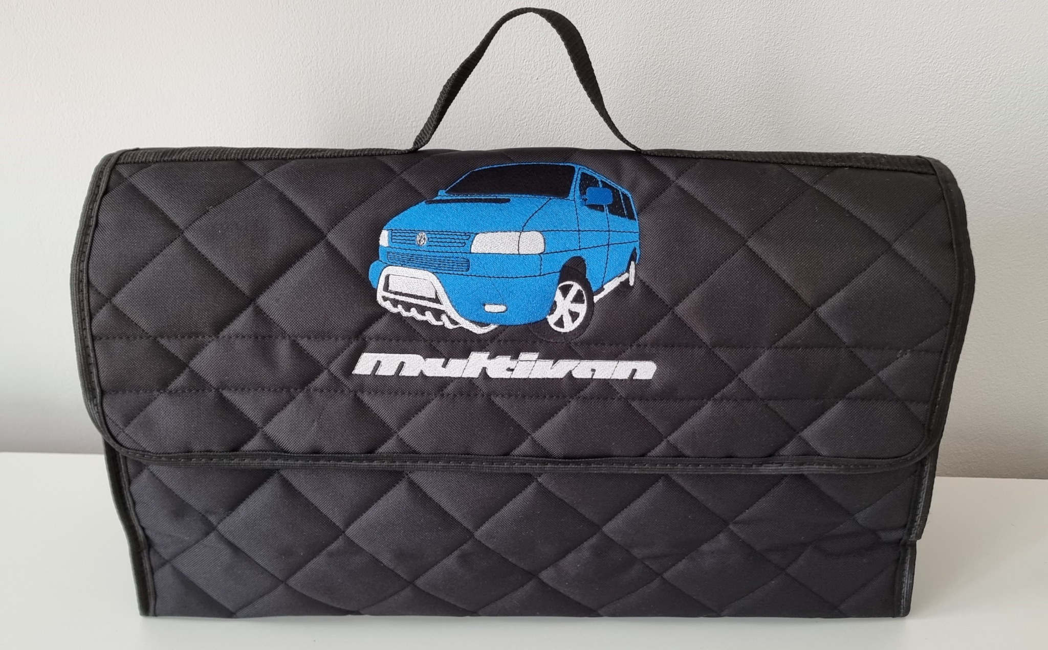 Czarna, pikowana torba z haftowanym niebieskim vanem i napisem 'Multivan'.