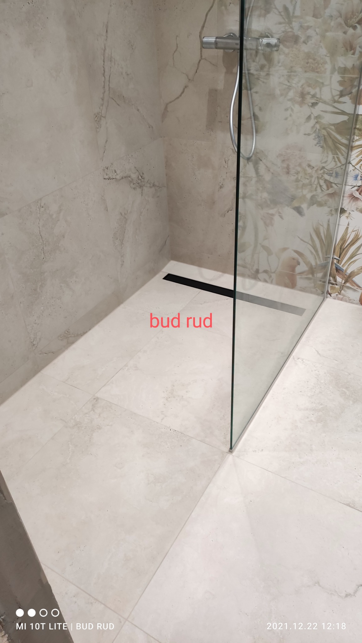 Wykończona kabina prysznicowa walk-in z odpływem liniowym, wyłożona beżowymi płytkami imitującymi marmur, widok z góry na szklaną ściankę i baterię prysznicową.