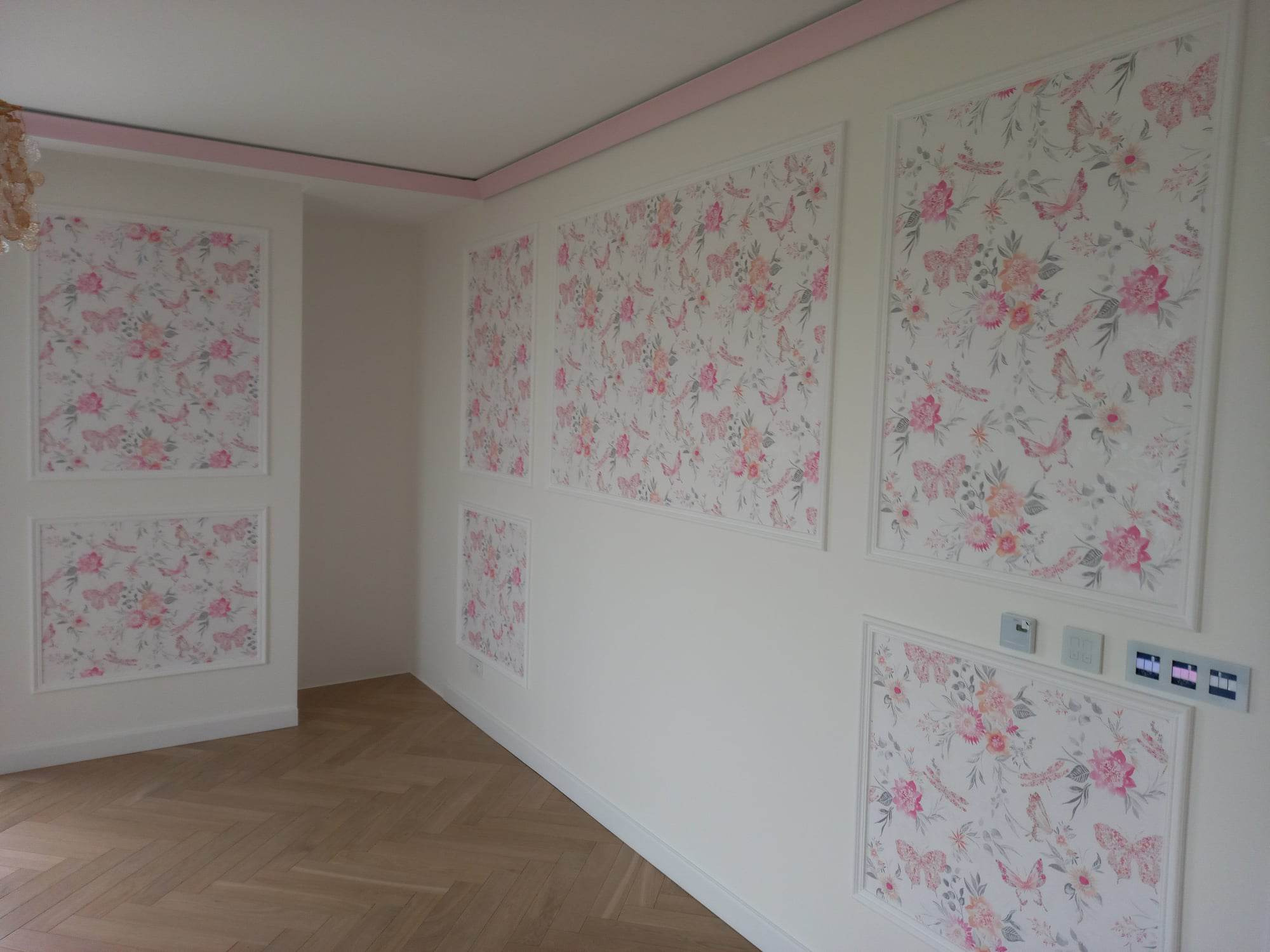 Pokój z tapetą w kwiaty i motyle w dekoracyjnych ramach, różowe akcenty na suficie, parkiet w jodełkę.