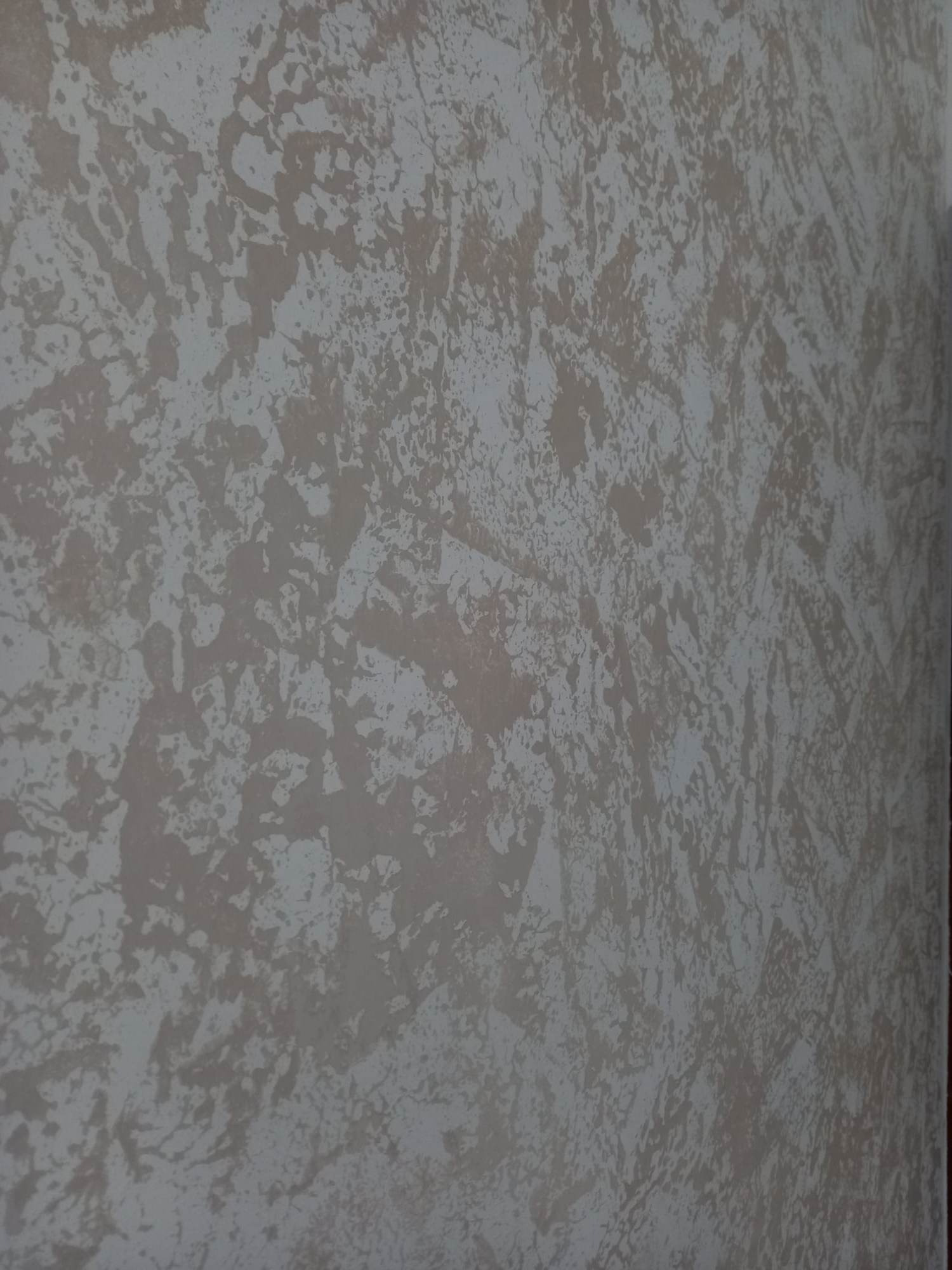 Ściana z dekoracyjną fakturą w odcieniach beżu i szarości, imitująca efekt marmuru lub kamienia, z widoczną strukturą i nieregularnymi wzorami.