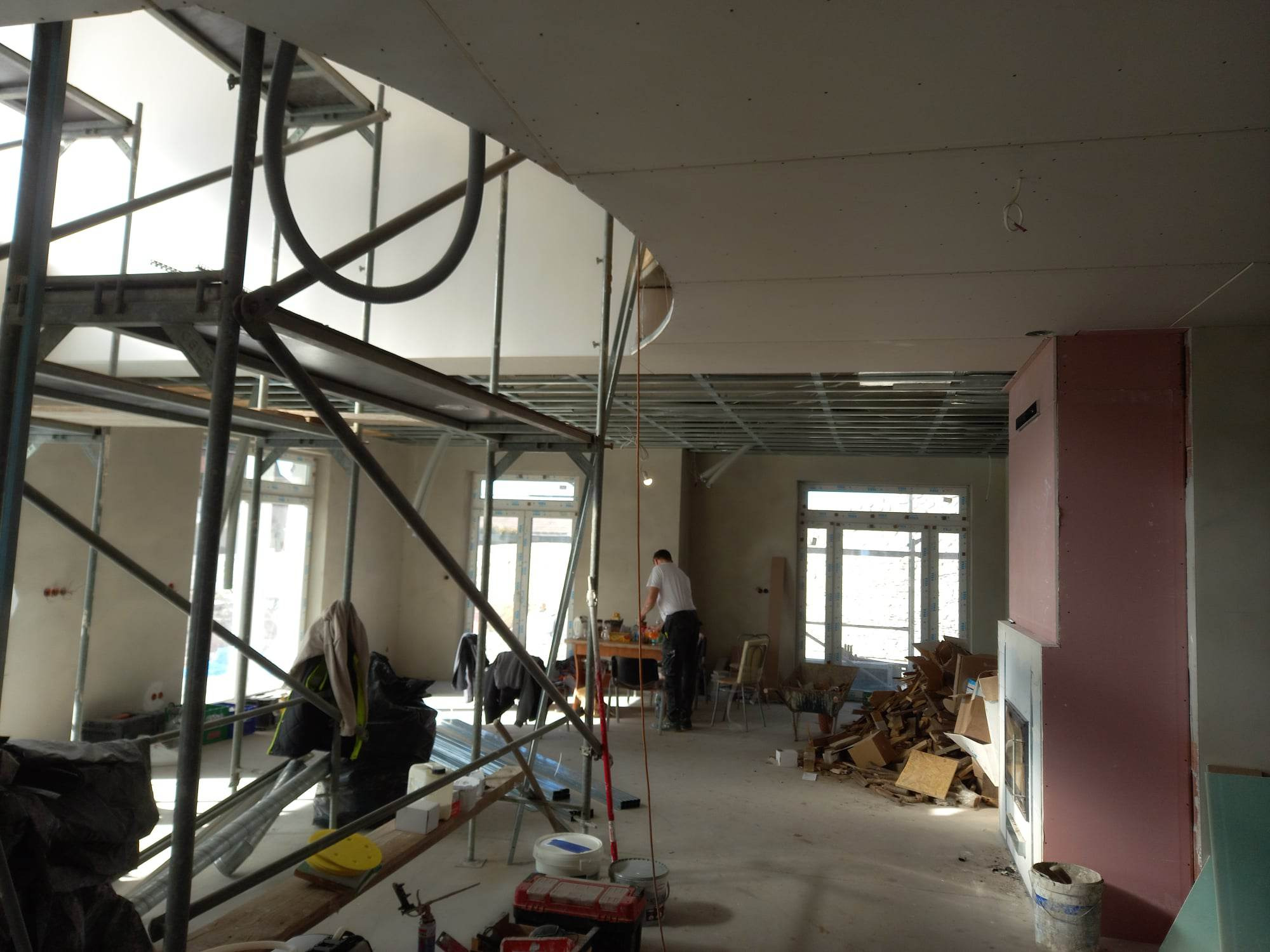 Wnętrze w trakcie montażu płyt karton gips na suficie, widoczne rusztowania, częściowo zabudowany kominek, bałagan budowlany.