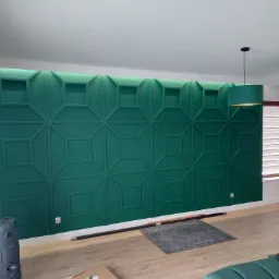 Szmaragdowa ściana dekoracyjna z podświetleniem LED na górze, wzór geometryczny kwadratów i rombów, fragment pokoju z lampą i podłogą drewnopodobną.