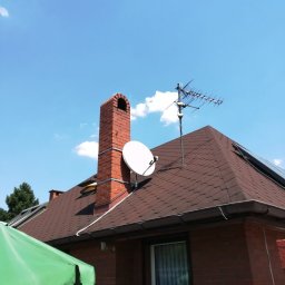 anteny serwis - Antena telewizyjna i satelitarna zamontowane na dachu domu z ceglanym kominem, widok z dołu na tle błękitnego nieba.