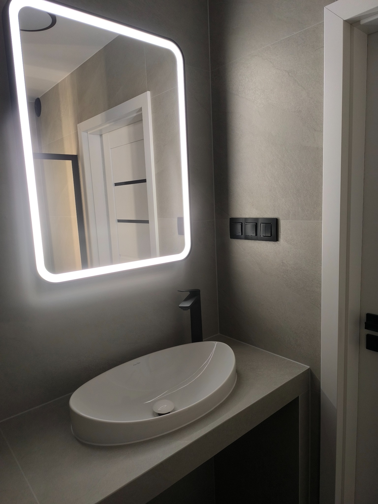 Nowoczesna łazienka z umywalką nablatową, podświetlanym lustrem i szarą okładziną ścienną.