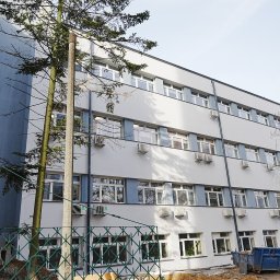 G&M+ sp. z o.o. - Odnowiony budynek biurowy z nową elewacją w odcieniach bieli i błękitu, widoczny z poziomu gruntu, z elementami zieleni i kontenerem na gruz w tle.