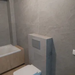 Nowoczesna łazienka z szarymi, matowymi płytkami imitującymi kamień, podwieszana toaleta z zabudowanym stelażem, obudowana wanna z drewnopodobną okładziną i jasna podłoga.