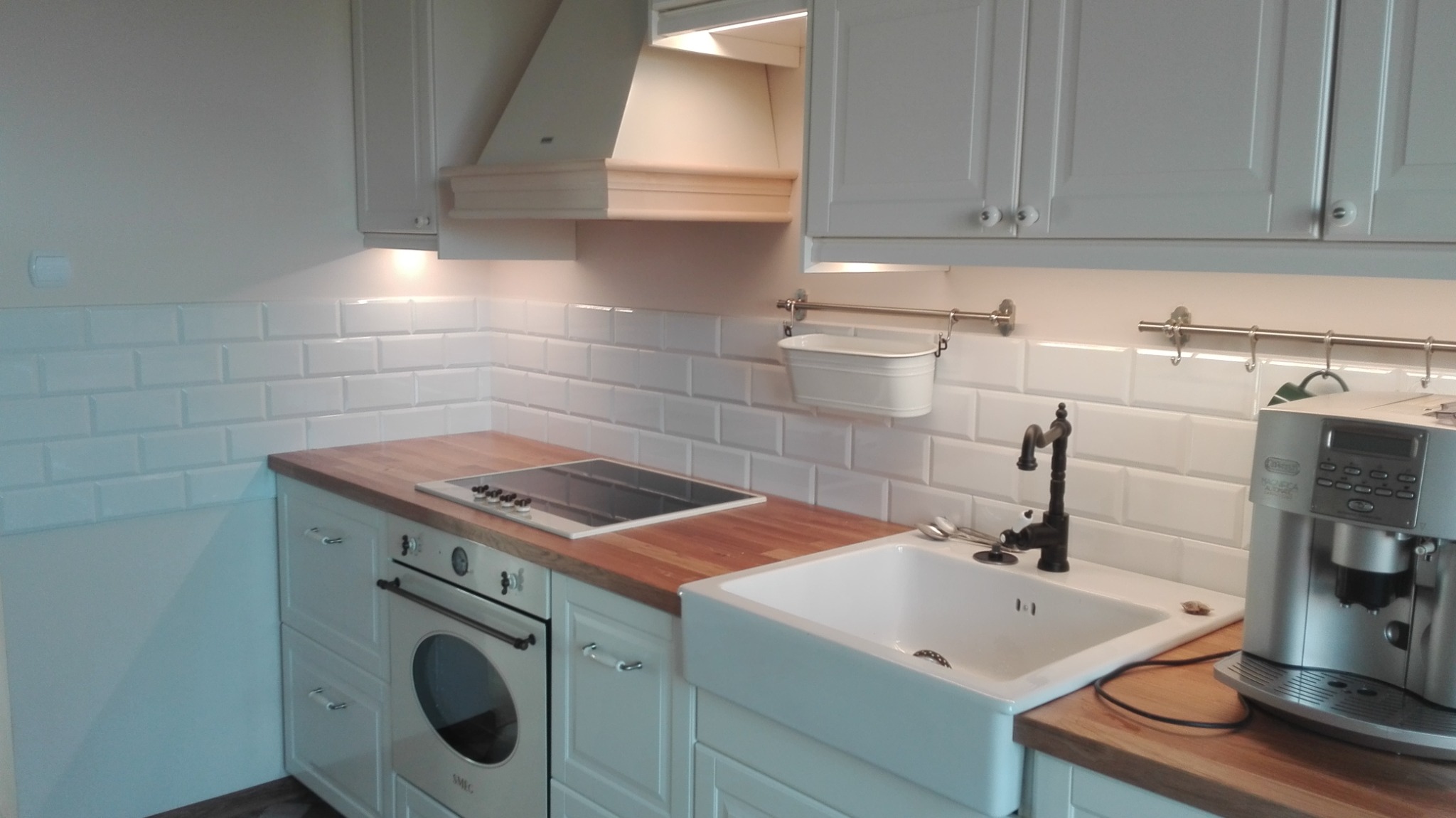 Kuchnia w stylu retro z białymi szafkami, drewnianym blatem, ceramicznym zlewem farmerskim i czarną armaturą, podświetlona listwami LED pod szafkami.