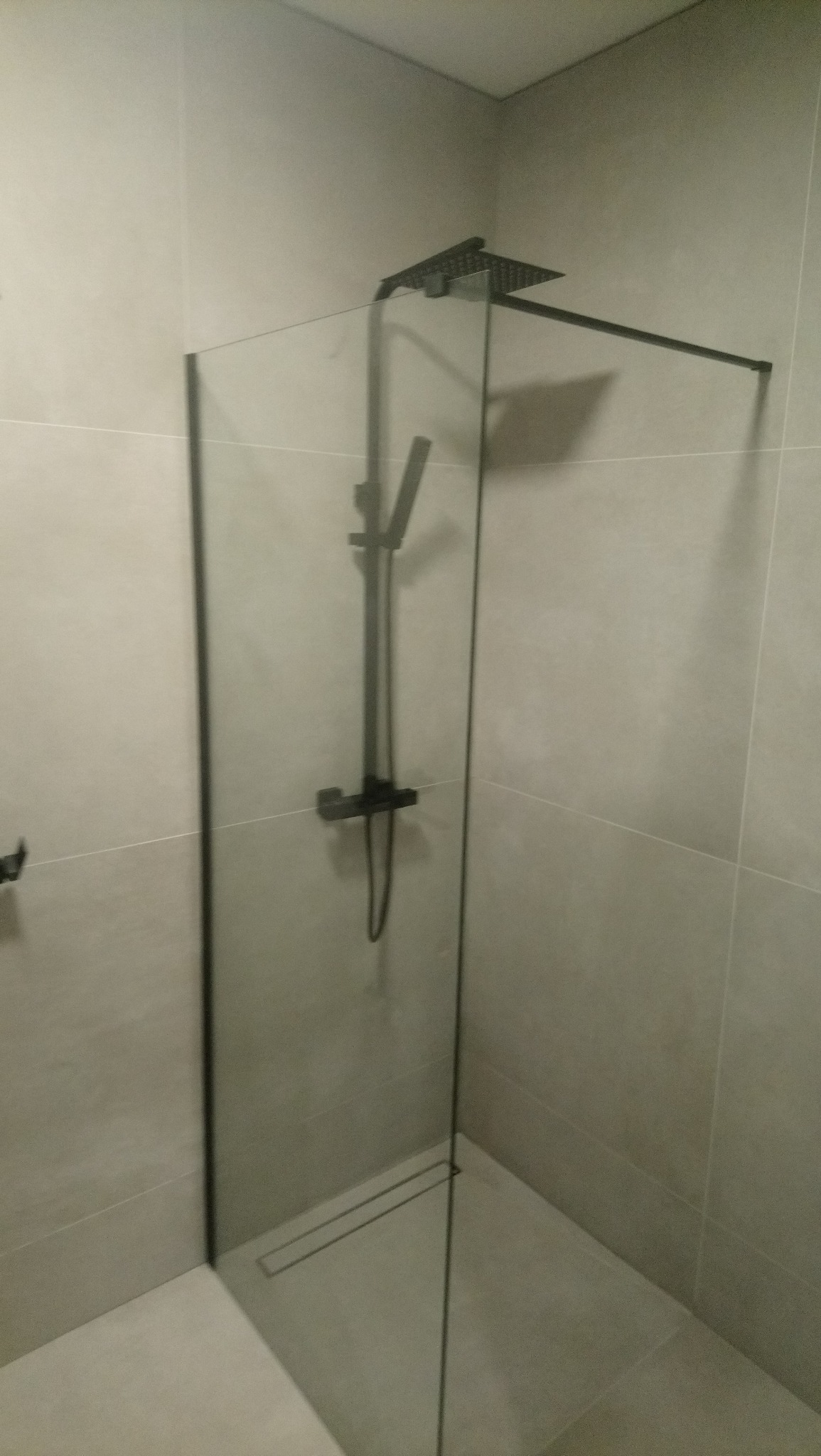 Nowoczesna kabina prysznicowa walk-in z czarną armaturą i odpływem liniowym, wykończona jasnymi płytkami.