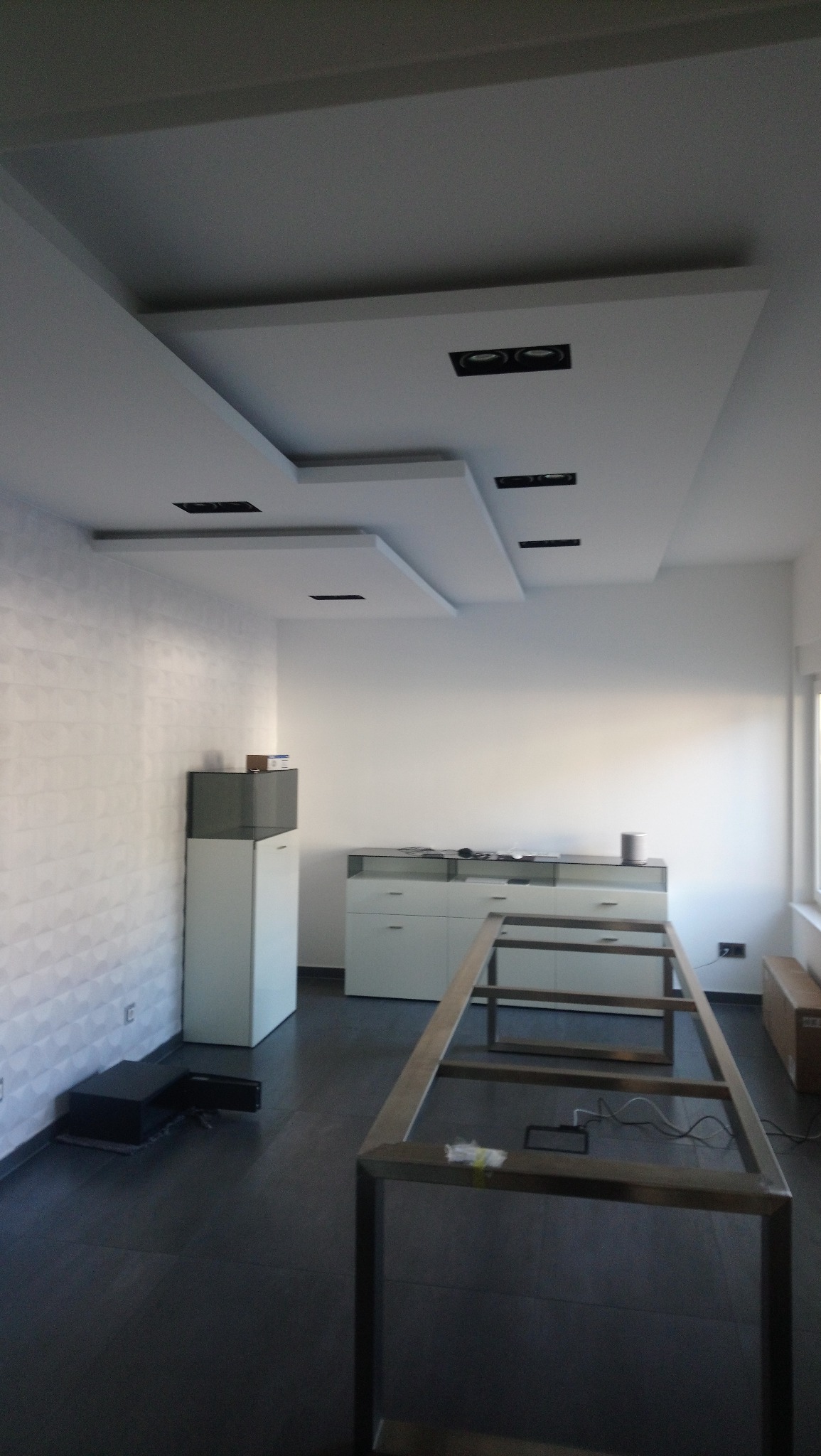 Wnętrze biura z podwieszanym sufitem z wbudowanym oświetleniem, białe meble biurowe i ciemna podłoga przed montażem stołu.