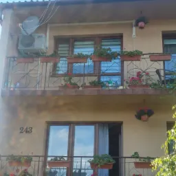 Elewacja dwupiętrowego domu z balkonami ozdobionymi kwiatami w donicach, klimatyzator na ścianie obok anteny satelitarnej