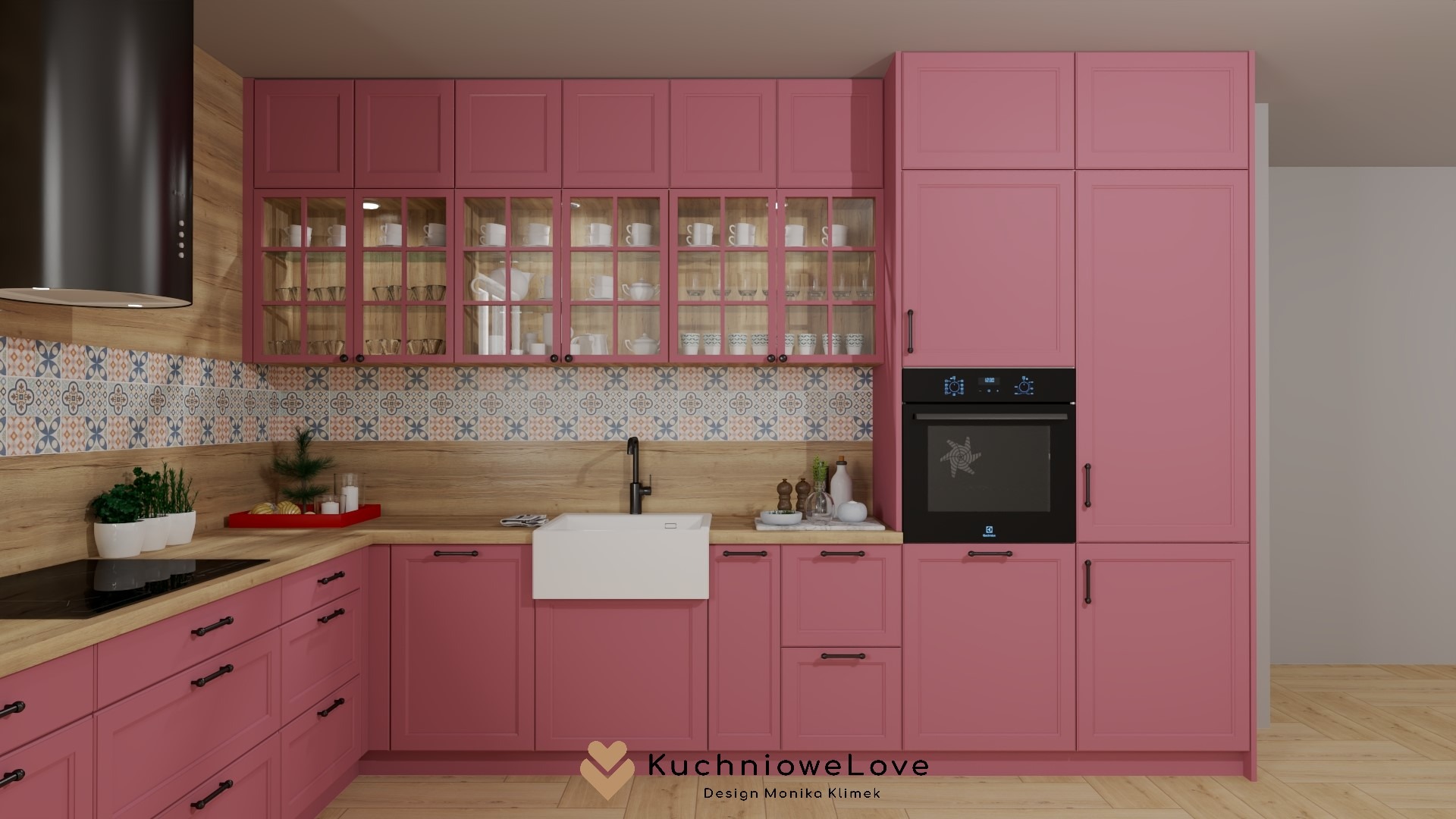 Różowa kuchnia z drewnianymi blatami i dekoracyjnymi płytkami ściennymi, czarny okap i biały zlew farmerski, szklane witryny z zastawą, projekt Monika Klimek.