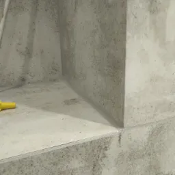 Wnęka w ścianie wyłożona szarą, wzorzystą glazurą, z widocznym żółtym elementem narzędzia po lewej stronie.