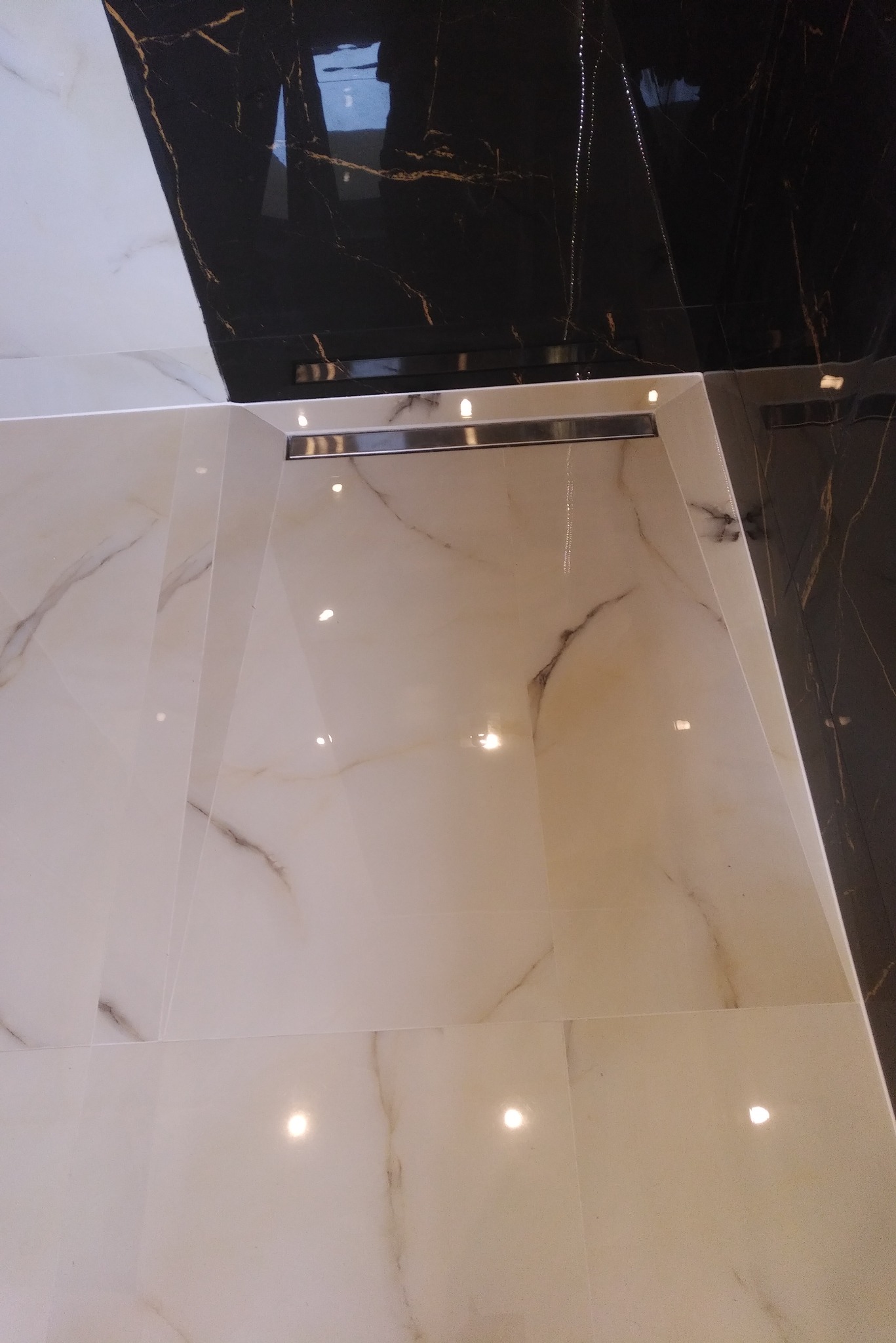 Białe i czarne marmurowe płytki podłogowe z odpływem liniowym ze stali nierdzewnej, połyskliwa powierzchnia odbija światło.