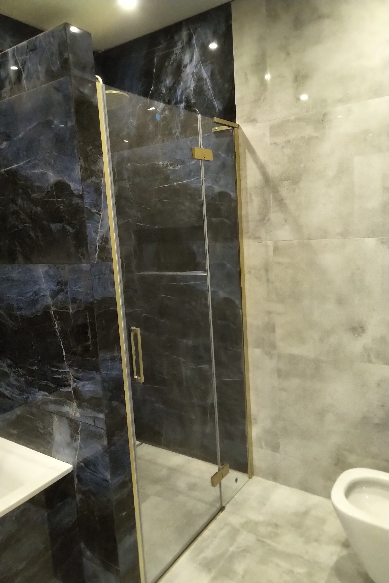 Nowoczesna kabina prysznicowa z marmurowymi płytkami w odcieniach szarości i niebieskiego, wykończona złotymi detalami, zrealizowana w Wojkowicach.