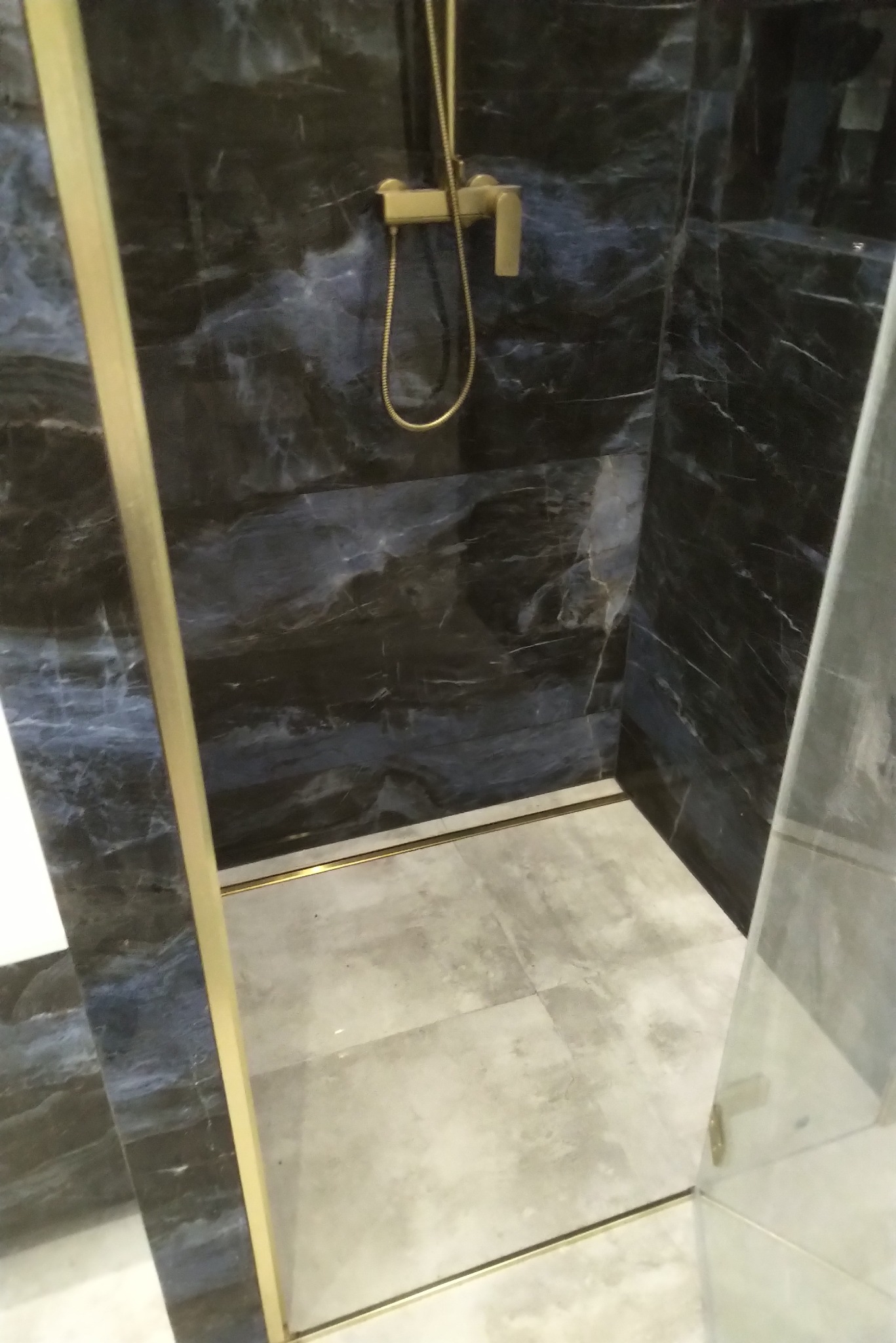 Nowoczesna kabina prysznicowa z czarnymi marmurkowymi płytkami, złotą armaturą i szklanymi drzwiami.