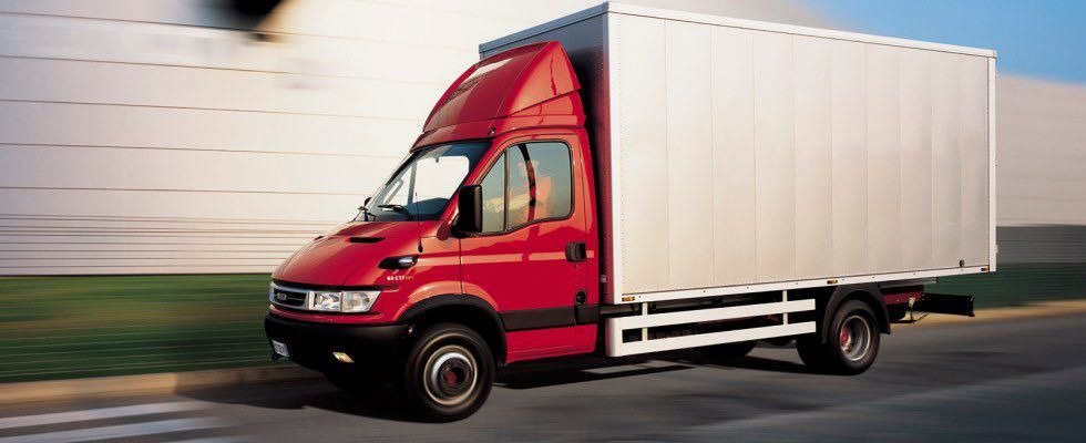 Czerwony samochód dostawczy z białą zabudową kontenerową, w ruchu, z efektem rozmycia tła, sugerującym szybką jazdę.