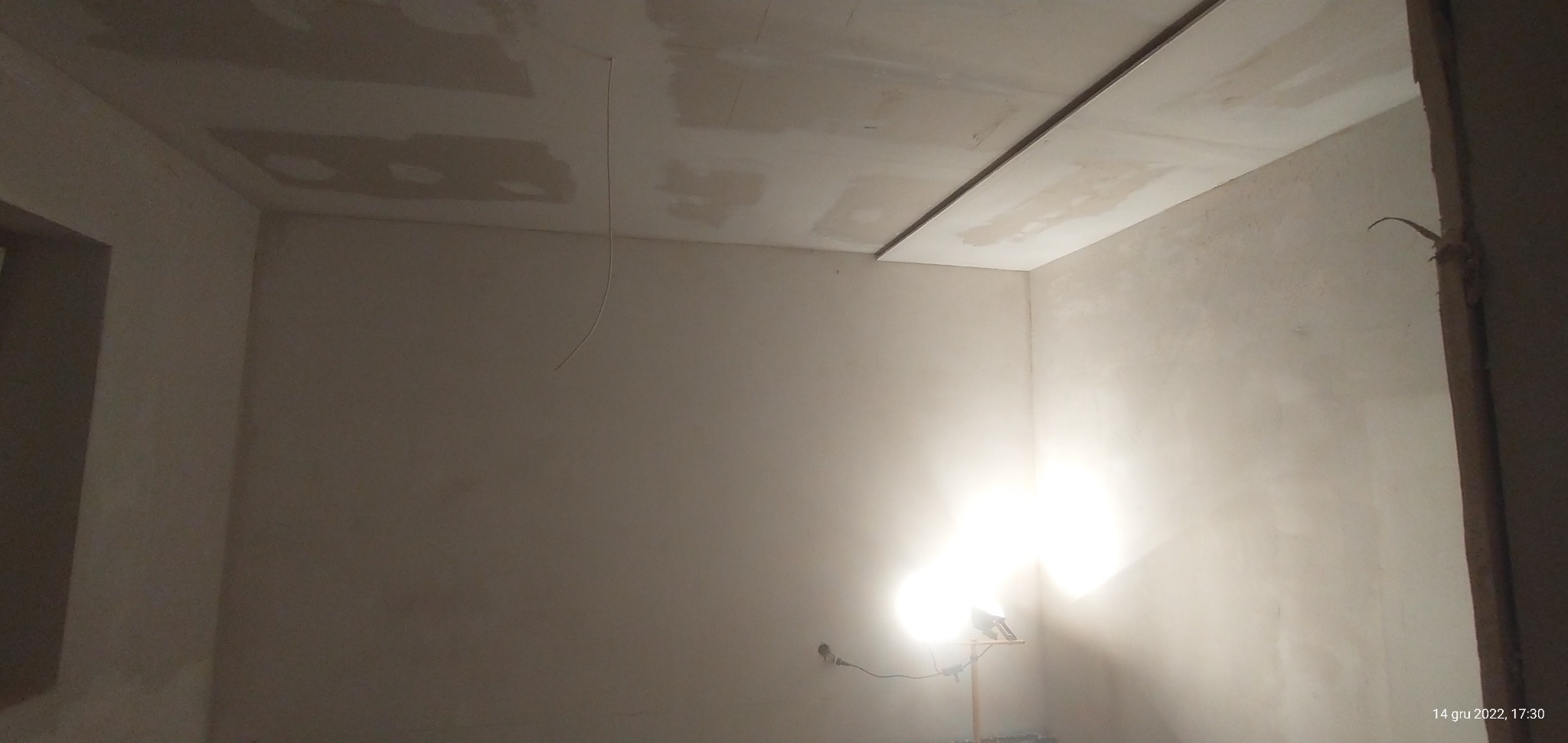 Pokój w trakcie prac wykończeniowych: częściowo zamontowany sufit podwieszany z płyt gipsowo-kartonowych, ściany wstępnie przygotowane pod malowanie, widoczne niedoskonałości i kabel zwisający...