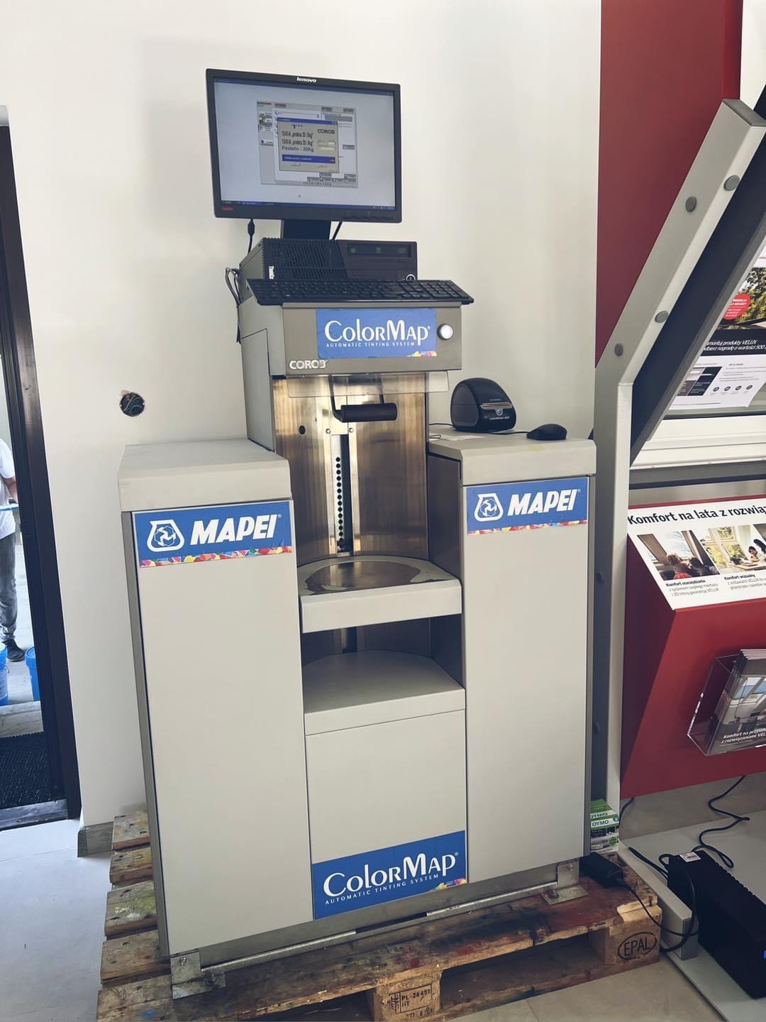 Automatyczny system barwienia ColorMap Corob na palecie, z monitorem pokazującym parametry, obok okna i materiałów reklamowych.