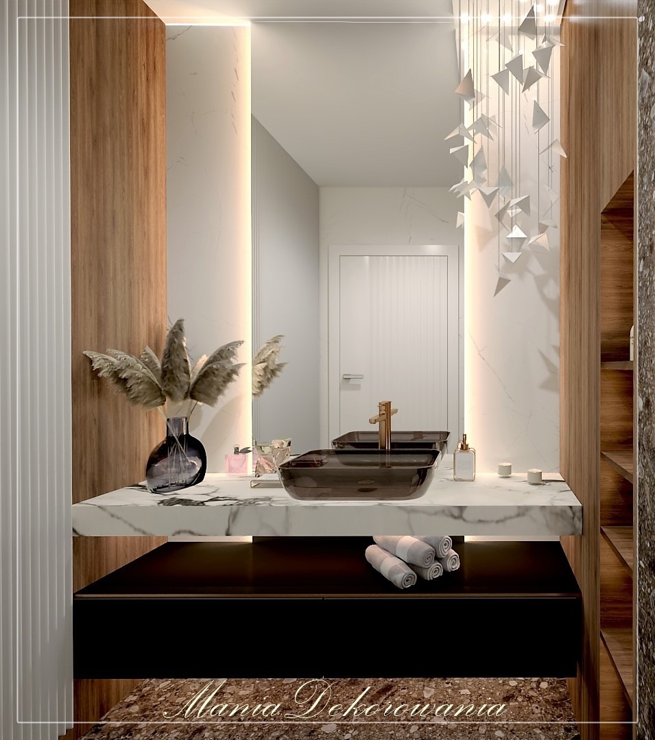 Elegancka łazienka z marmurowym blatem, umywalką z ciemnego szkła i złotą armaturą, oświetlona dekoracyjną lampą wiszącą i podświetleniem lustra.