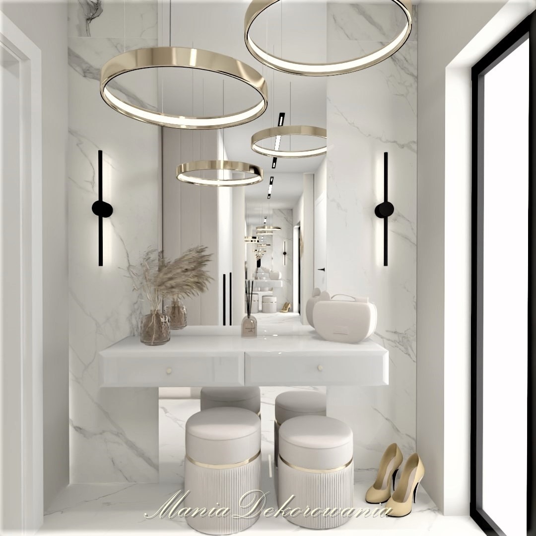 Elegancka toaletka w łazience wykończonej marmurem, z okrągłymi lampami wiszącymi i dwoma stołkami obitymi kremową skórą. Para beżowych szpilek stoi obok stołków.