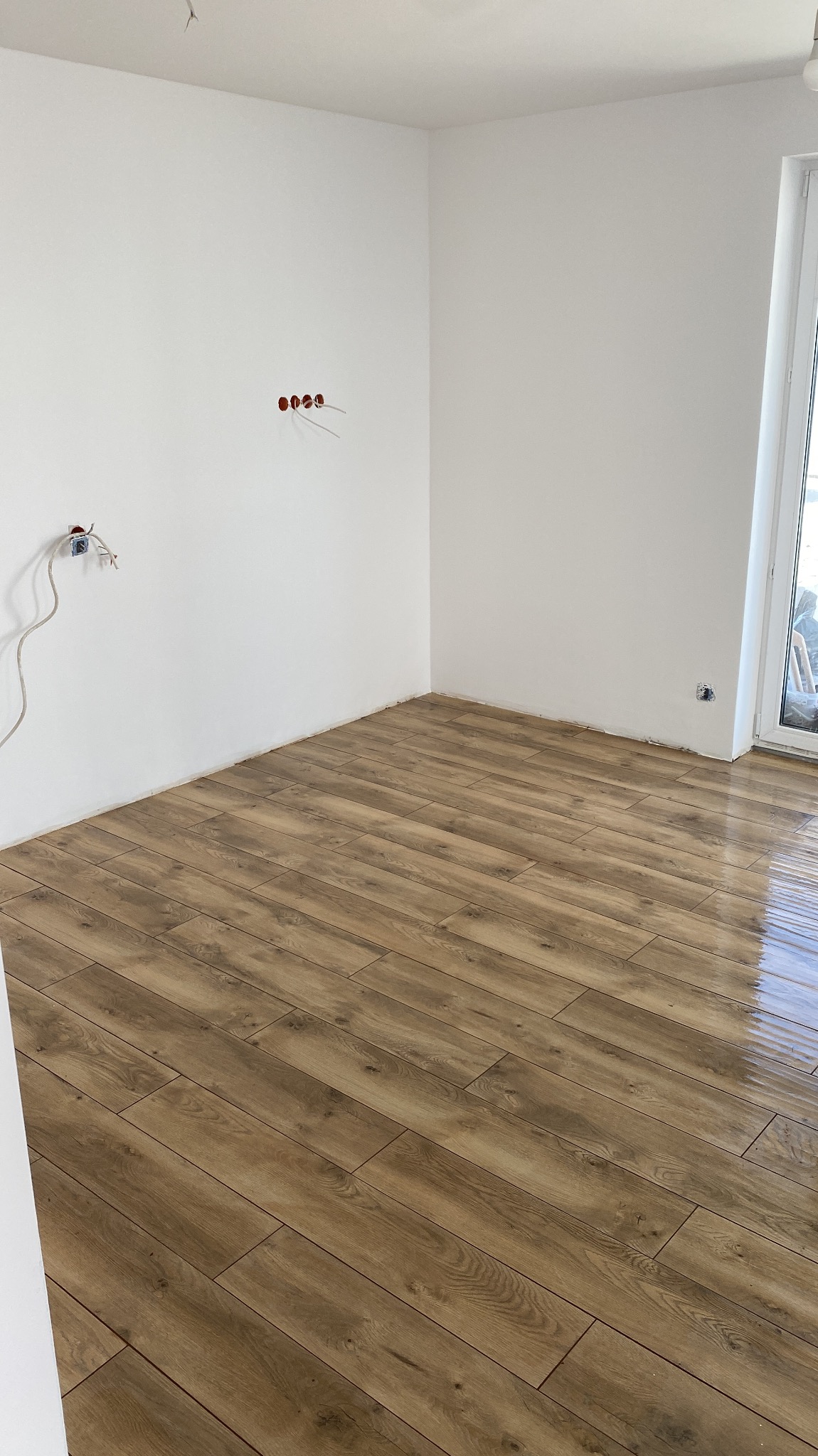 Ułożona podłoga z płytek imitujących drewno w nowym pomieszczeniu z białymi ścianami i wystającymi kablami elektrycznymi.