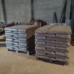 Dwa stosy worków z pelletem ułożone na paletach w magazynie o surowych, betonowych ścianach. Worki są przezroczyste, ukazując zawartość.