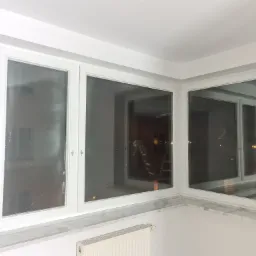 Trzyczęściowe białe okno z marmurowym parapetem, widoczne odbicie drabiny w szybie, nocny widok za oknem.