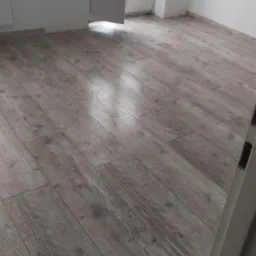 Ułożona podłoga z paneli imitujących drewno w nowym, jasnym pokoju z balkonem i grzejnikiem, widok z góry.