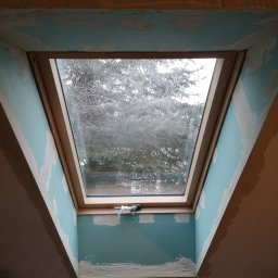 Robert chłodziński renbud - Montaż okna dachowego w trakcie wykańczania wnęki przy użyciu płyty kartonowo-gipsowej; widoczne niedoskonałości w szpachlowaniu i przygotowaniu do malowania.