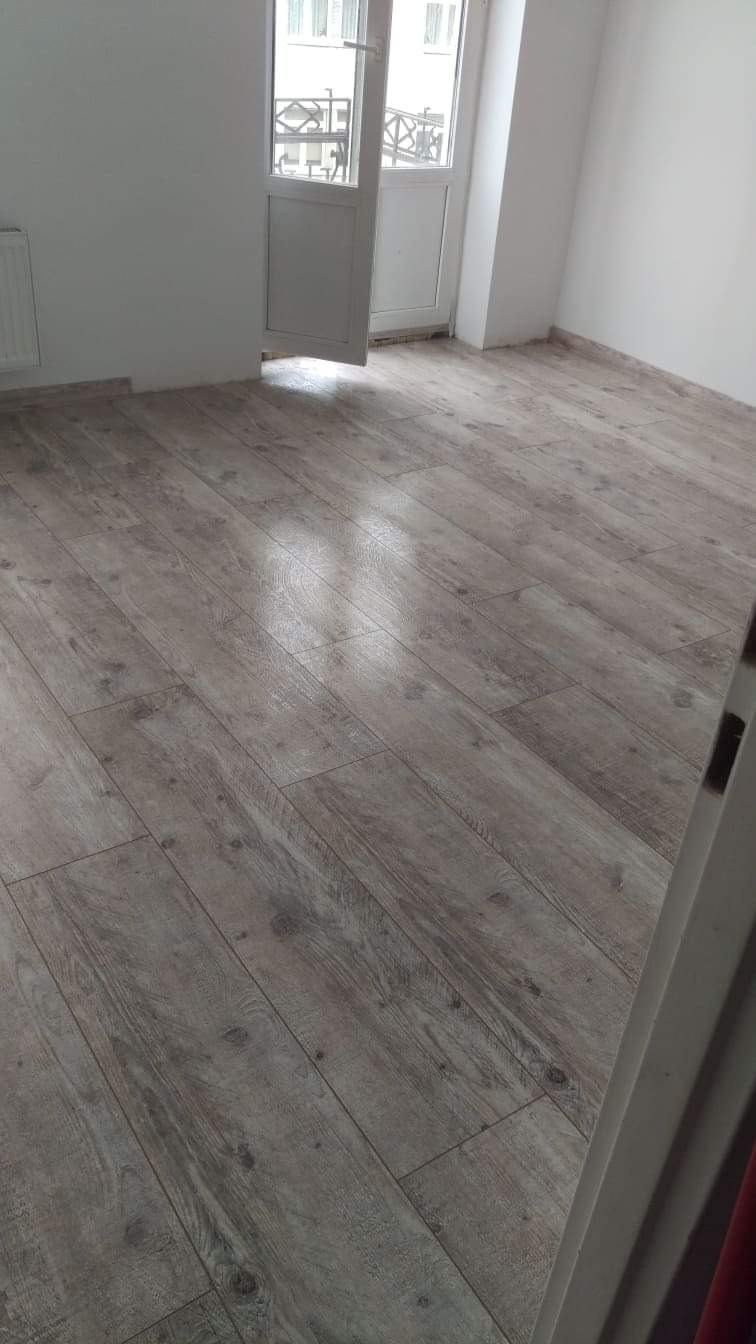 Ułożona podłoga z paneli imitujących drewno w nowym, jasnym pokoju z balkonem i grzejnikiem, widok z góry.