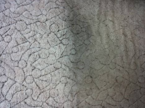 Szaro-beżowa powierzchnia dywanu z geometrycznym wzorem, widoczne delikatne cienie i nierówności struktury włókien.