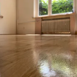 Błyszcząca, świeżo polakierowana podłoga z parkietu dębowego w jasnym pomieszczeniu z oknem i grzejnikiem.