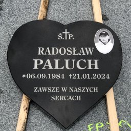 MARSTONE ANTKOWIAK BARBARA - Czarny nagrobek w kształcie serca z wygrawerowanym imieniem, nazwiskiem, datami urodzin i śmierci oraz zdjęciem osoby, oparty o drewniane podpórki na szarym, kamiennym tle.