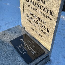 MARSTONE ANTKOWIAK BARBARA - Granitowy nagrobek z wygrawerowanymi imionami i datami, częściowo pokryty śniegiem, w słoneczny dzień na cmentarzu. Widoczny krzyż i napis 'Ave Maria'.