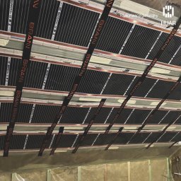 HUAR spółka z ograniczoną odpowiedzialnością - Montaż folii grzewczej na podłodze, widoczne pasy folii z napisem 'BRAIN' przymocowane taśmą, przygotowane do dalszych prac wykończeniowych.